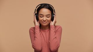 a girl in a pink jumper holding he rhands over her headphones with her eyes closed