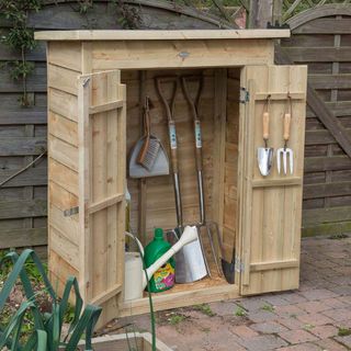 Double door storage unit with hooks and small garden spade and fork hanging on it