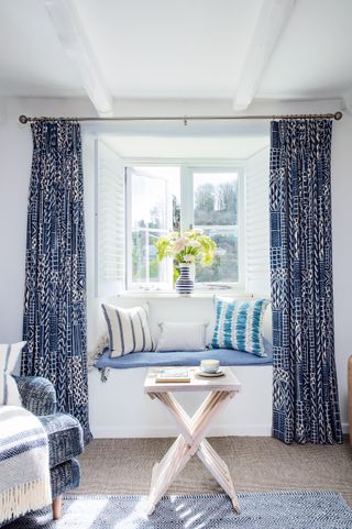 Living room detail with folding table in front of window seat and blue and white curtains