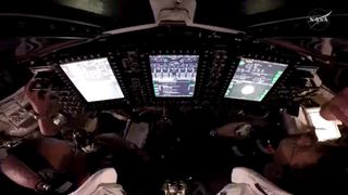 A look into a dark cockpit with three bright white computer screens