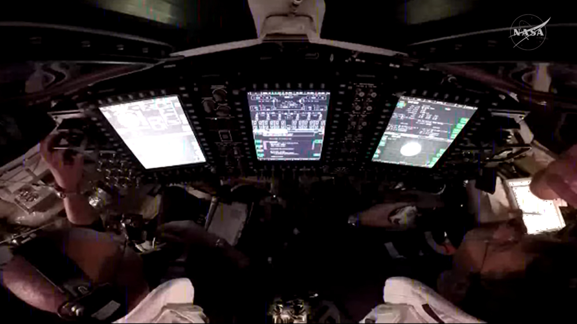 A look into a dark cockpit with three bright white computer screens