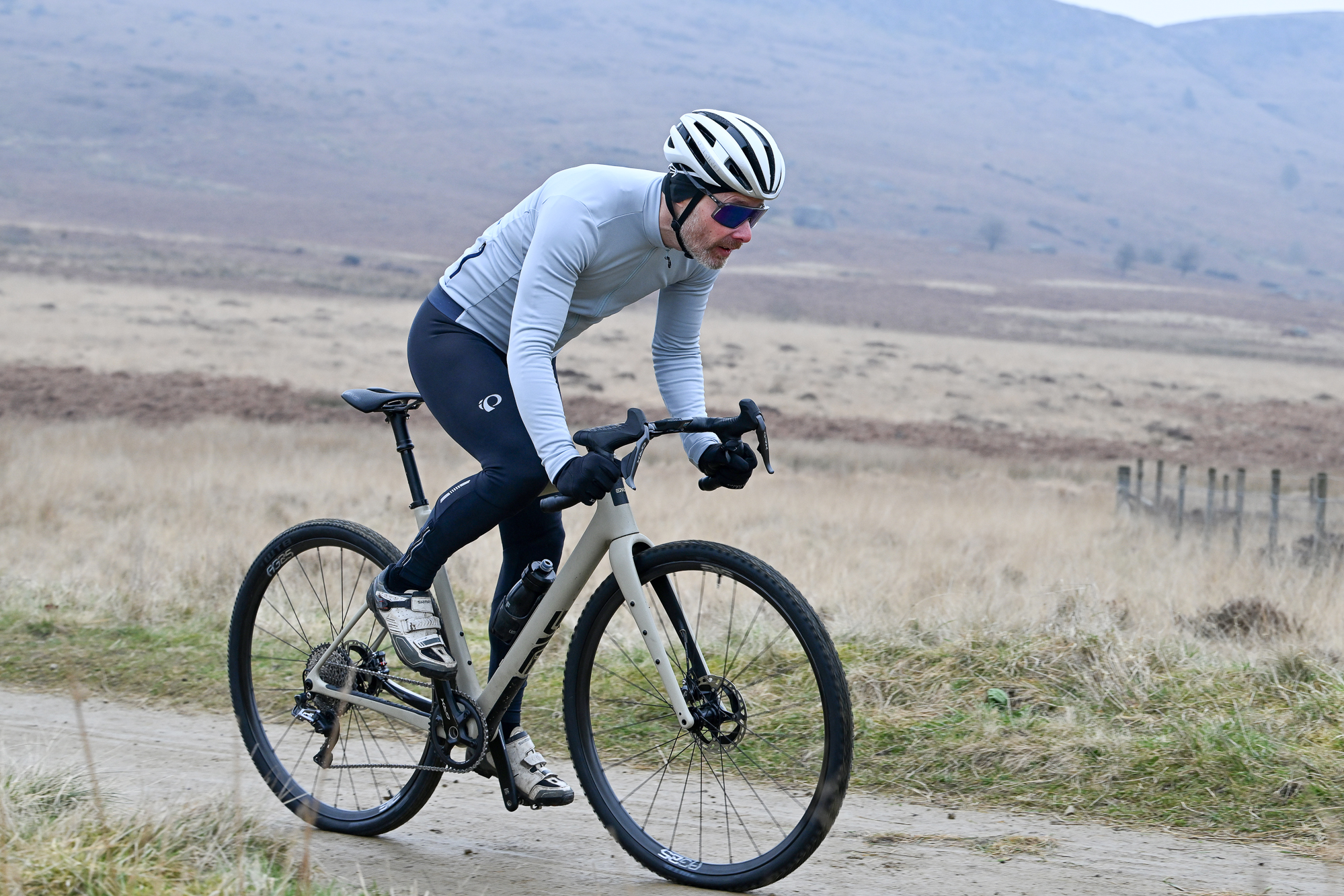 Man in a blue jersey riding a gravel bike out of the saddle on a smooth, sandy trail