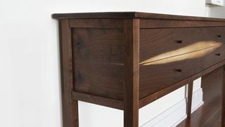 Close up view of a wooden two drawer console table in a space with white walls and wood flooring