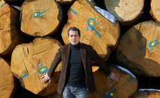 A portrait of Andrea Margaritelli standing in front of large logs.