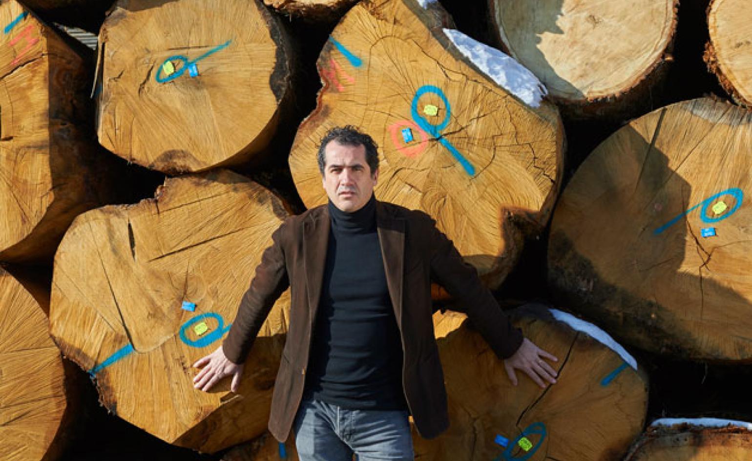 A portrait of Andrea Margaritelli standing in front of large logs.