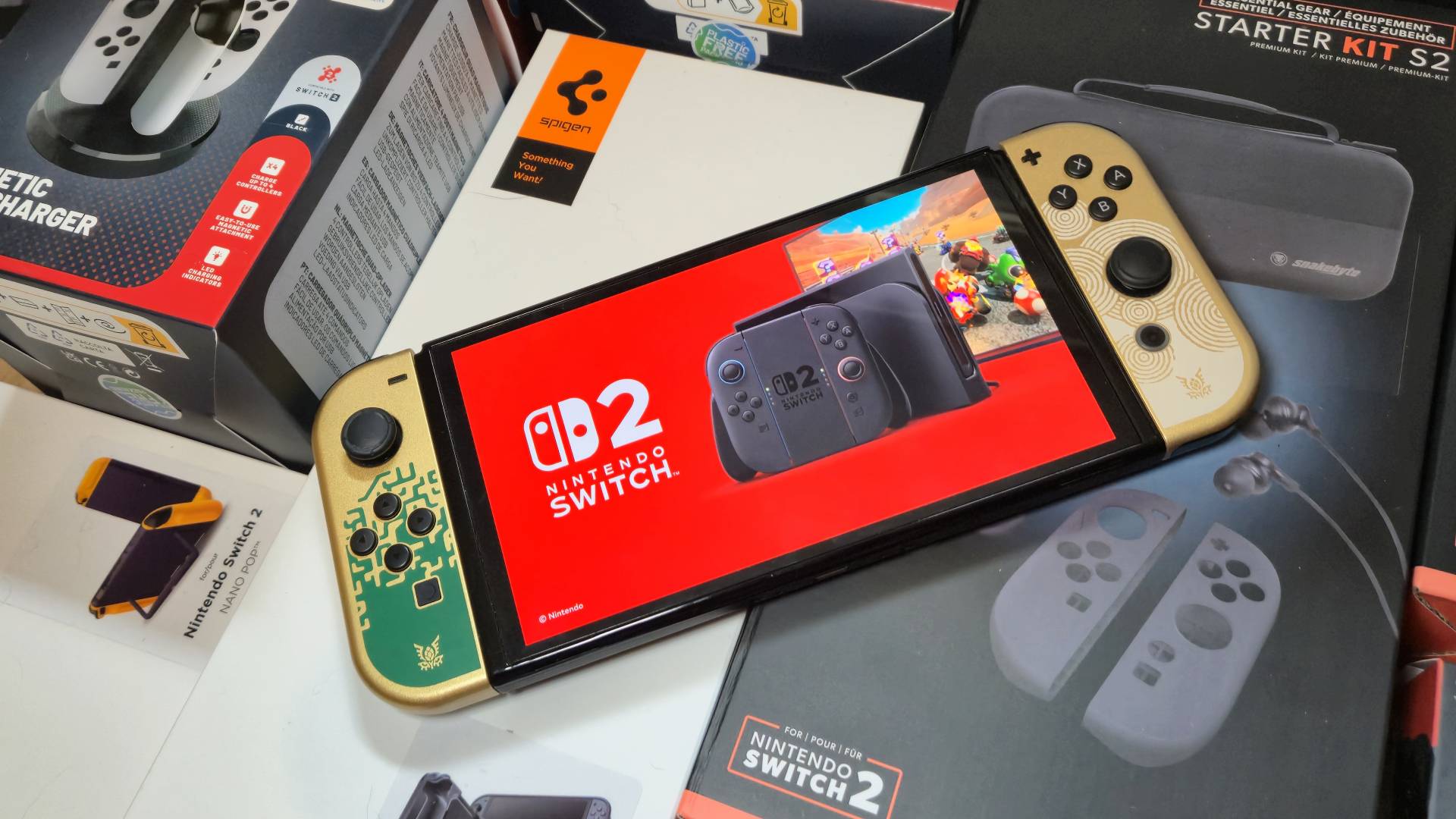 Photo of an OLED Nintendo Switch displaying the Switch 2, sitting on a pile of Switch 2 accessories by Spigen, Snakebyte and STEALTH.