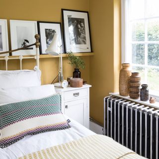 Yellow bedroom with white bedding and a silver radiator on the wall under a window