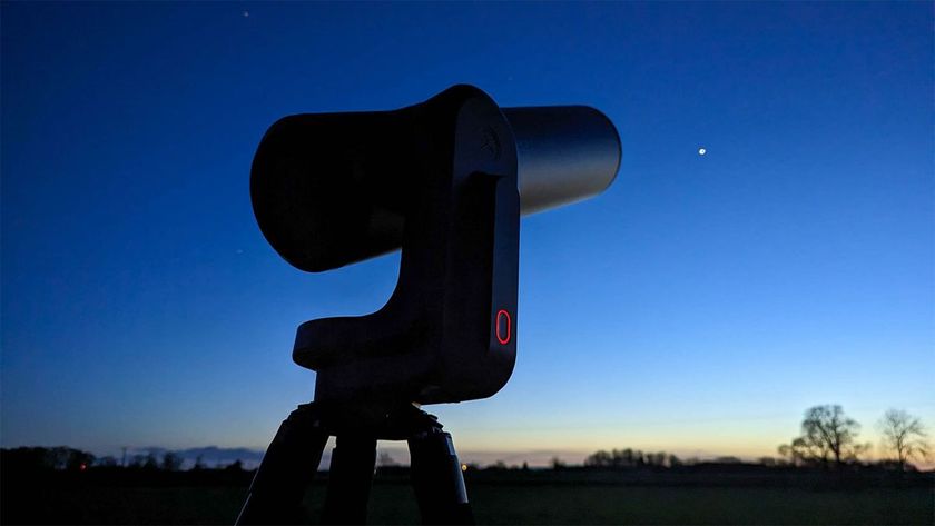 The unistellar eQuinox 2 telescope is a dark metallic colour and it looks up at the evening sky, which is a dark blue with light setting on the horizon