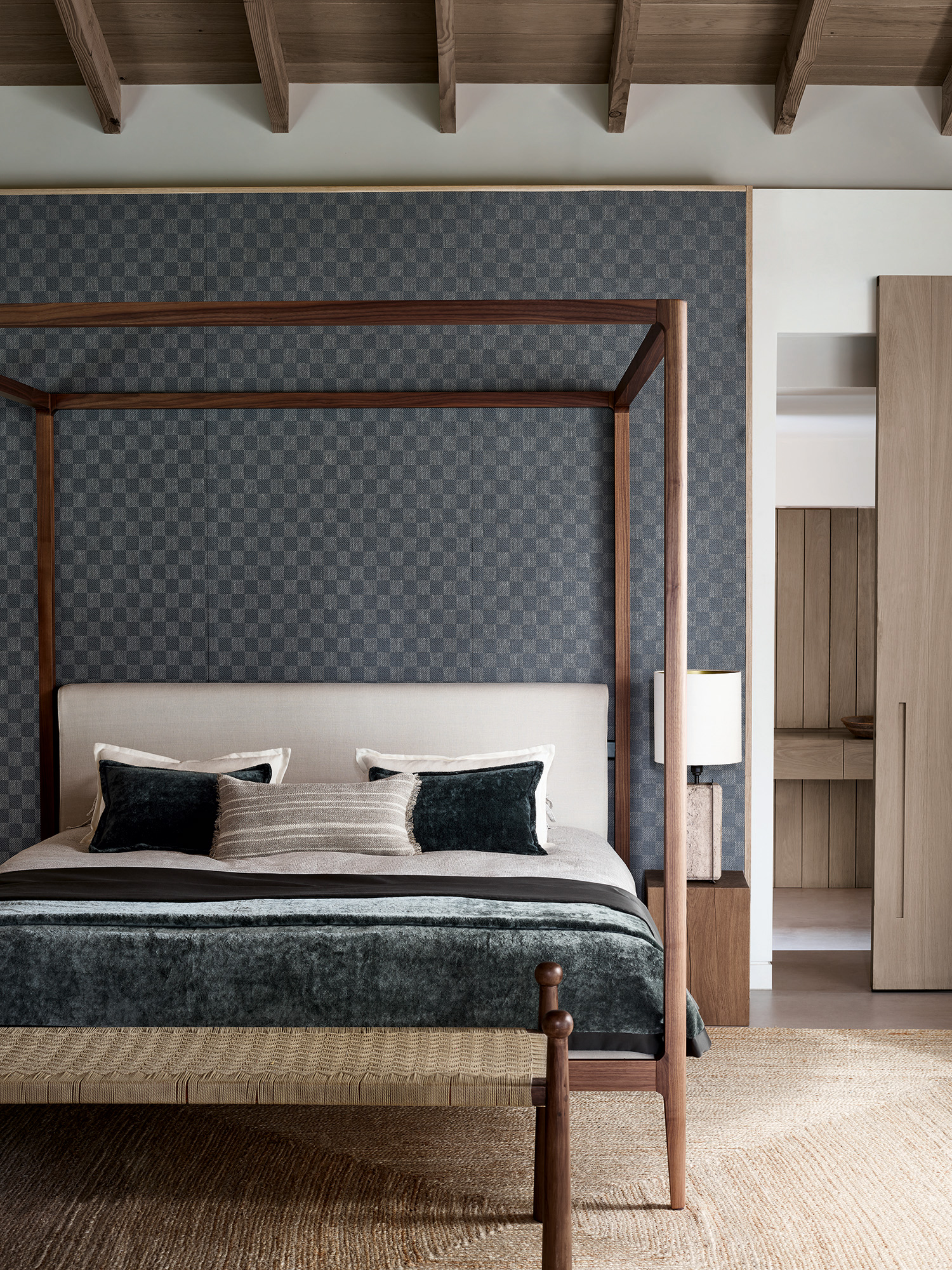 grey and white bedroom with grey check wall covering, four poster bed, coir rug, wicker footstool