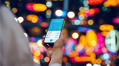 A woman looks at her phone against the backdrop of nighttime city lights.