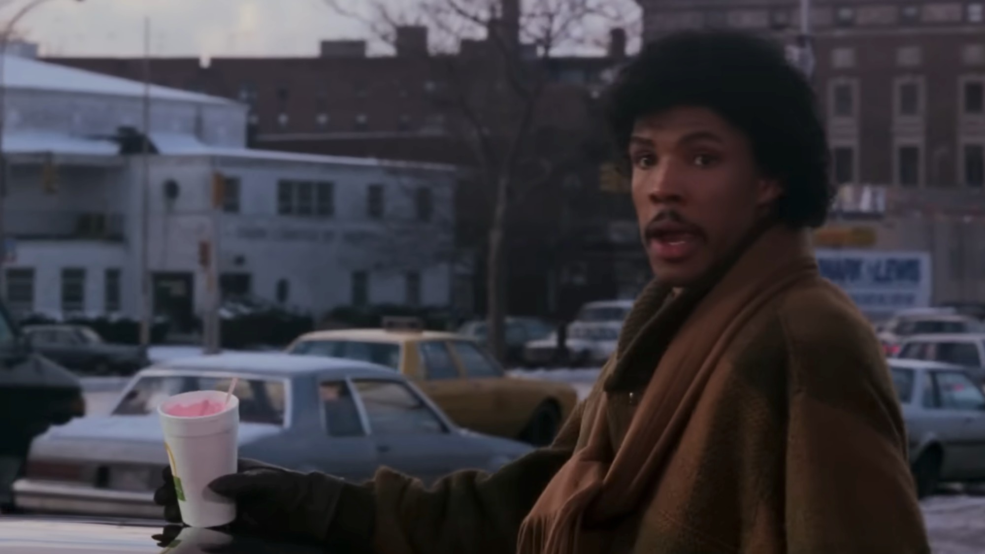 Eriq La Salle holding a strawberry milkshake and looking past the camera in Coming to America