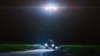 a pickup truck in a field at night, with the bright lights of a strange craft above it.
