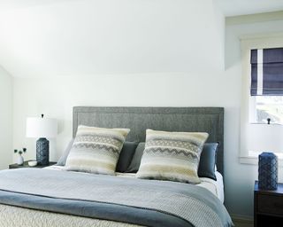 Bright white bedroom with blue accents, dark gray upholstered headboard, blue and white bedding, matching bedside lamps, matching blue and white blinds