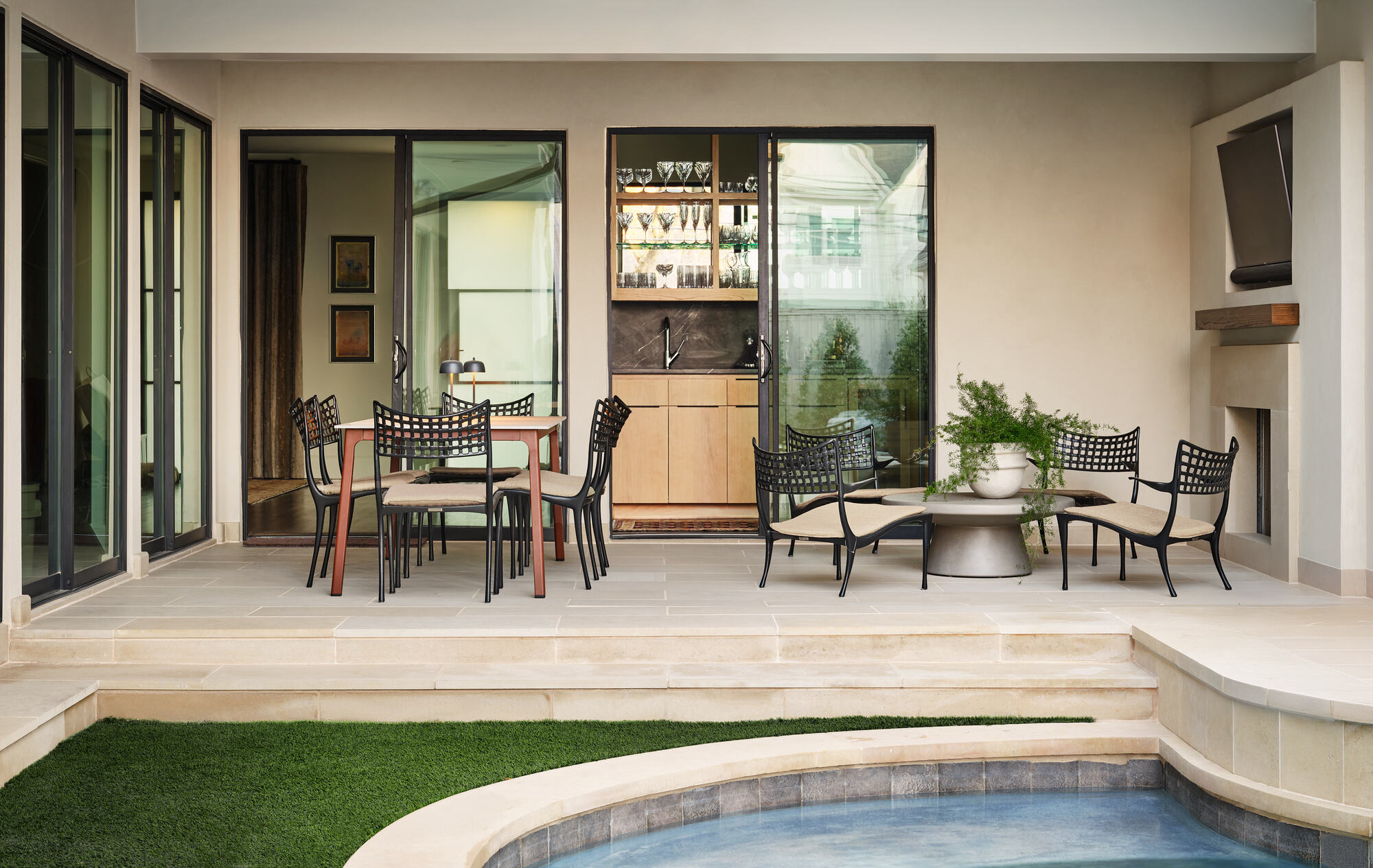 outdoor dining area with dining table and chairs, a separate seating area around a circle coffee table, steps down to a lawn and swimming pool