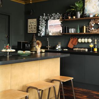 Black kitchen with gold island, bar stools and wooden shelves on wall