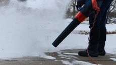 A person is using a corded leaf blower to blow snow from their driveway
