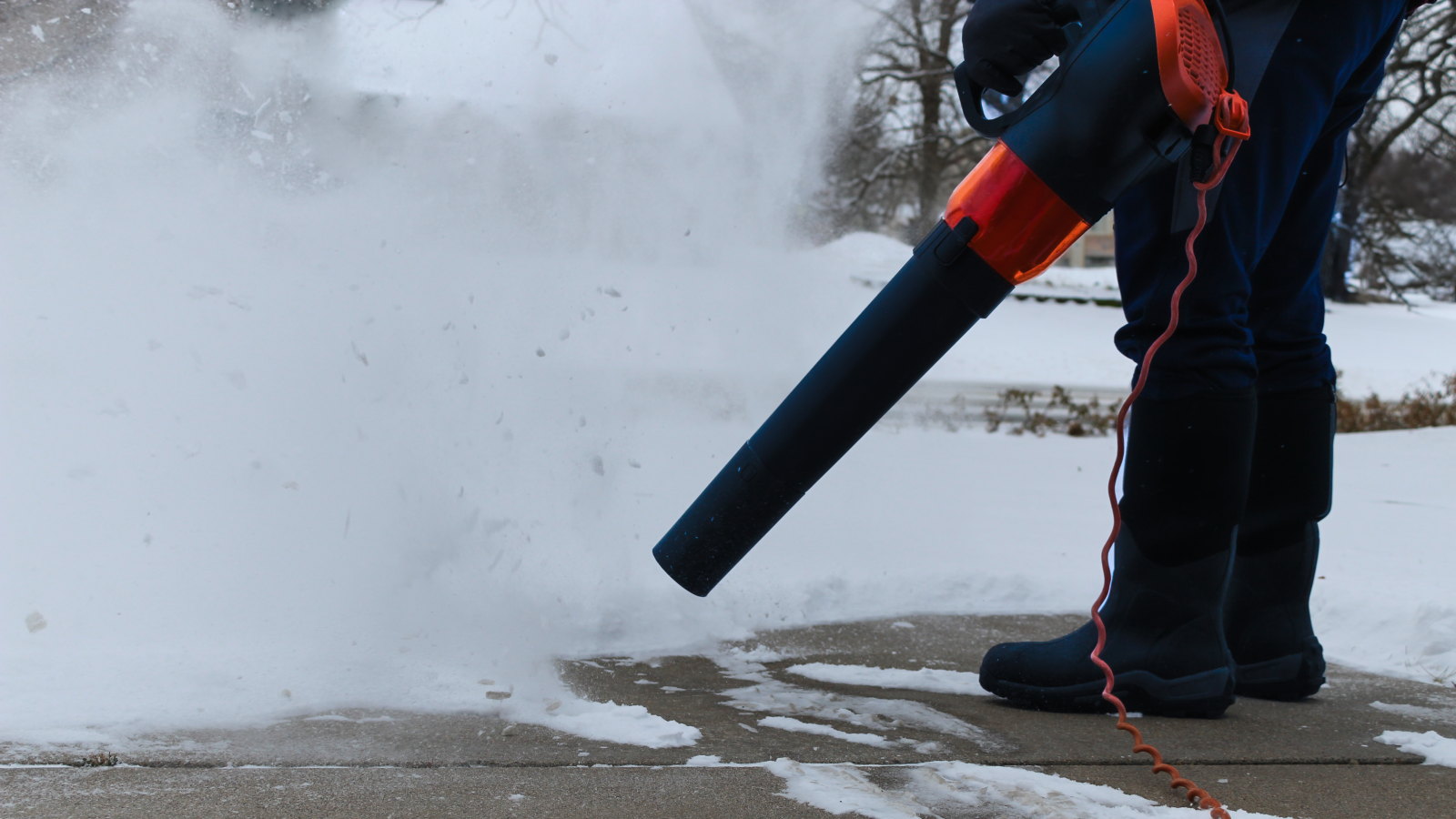 A person is using a corded leaf blower to blow snow from their driveway