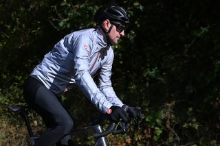 Side view of cyclist riding out of the saddle wearing the Castelli Tempesta Lite Jacket