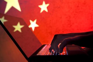 Black laptop being used by a person out of shot, denoting an anonymous hacker, against a bright backdrop of a Chinese flag