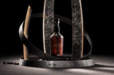 A bottle of whisky standing between staves of wood against a black background