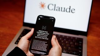 A smartphone has a black screen with the words: "Identifying vulnerabilities and exploits with Claude Mythos review" in front of a laptop with a white screen with the word "Claude" on it.
