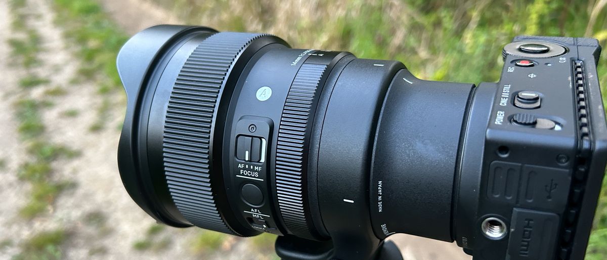 A black camera lens with two ridged adjustment rings is mounted to an out-of-frame tripod and attached to a rectangular black camera.