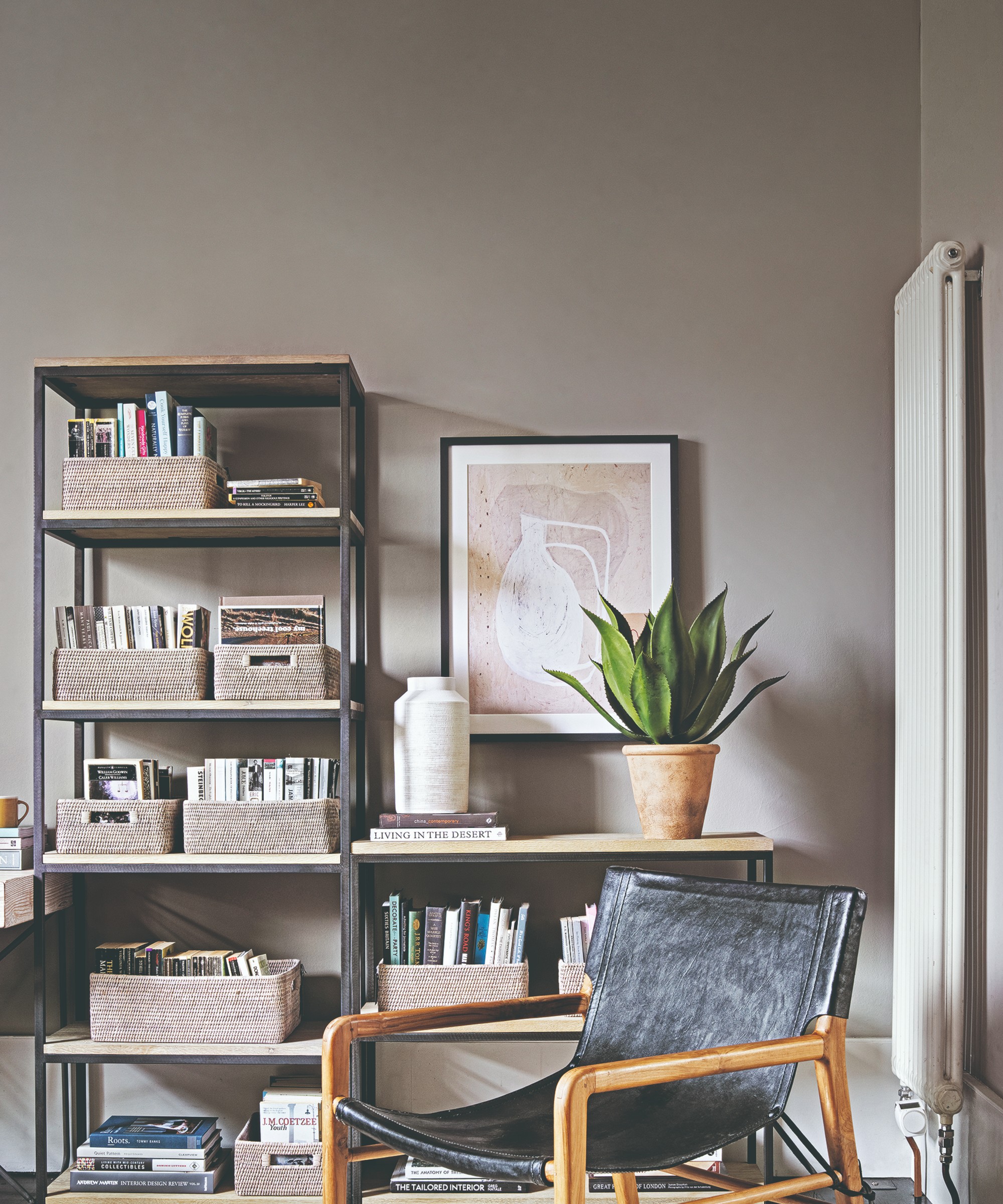 A grey living room with bookshelves filled with books in storage baskets and a black leather accent chair