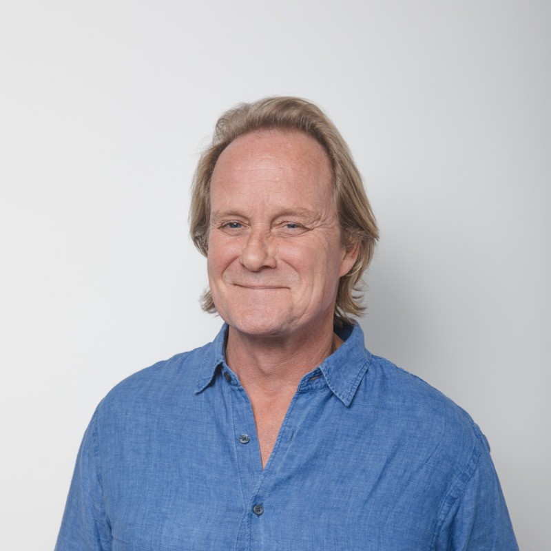 Headshot of a middle-aged man with blonde hair, wearing a blue linen shirt and smiling at the camera