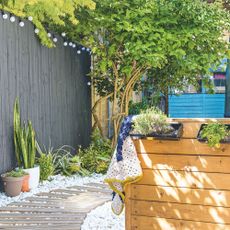 Garden area with a wooden decked path surrounded by stones and plants growing up the black painted fence