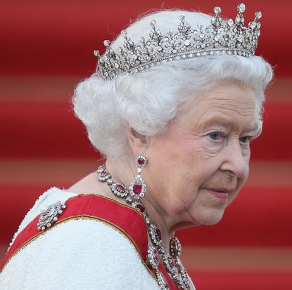 Queen Elizabeth wearing ruby and diamond jewelry, a white dress, red sash and diamond tiara