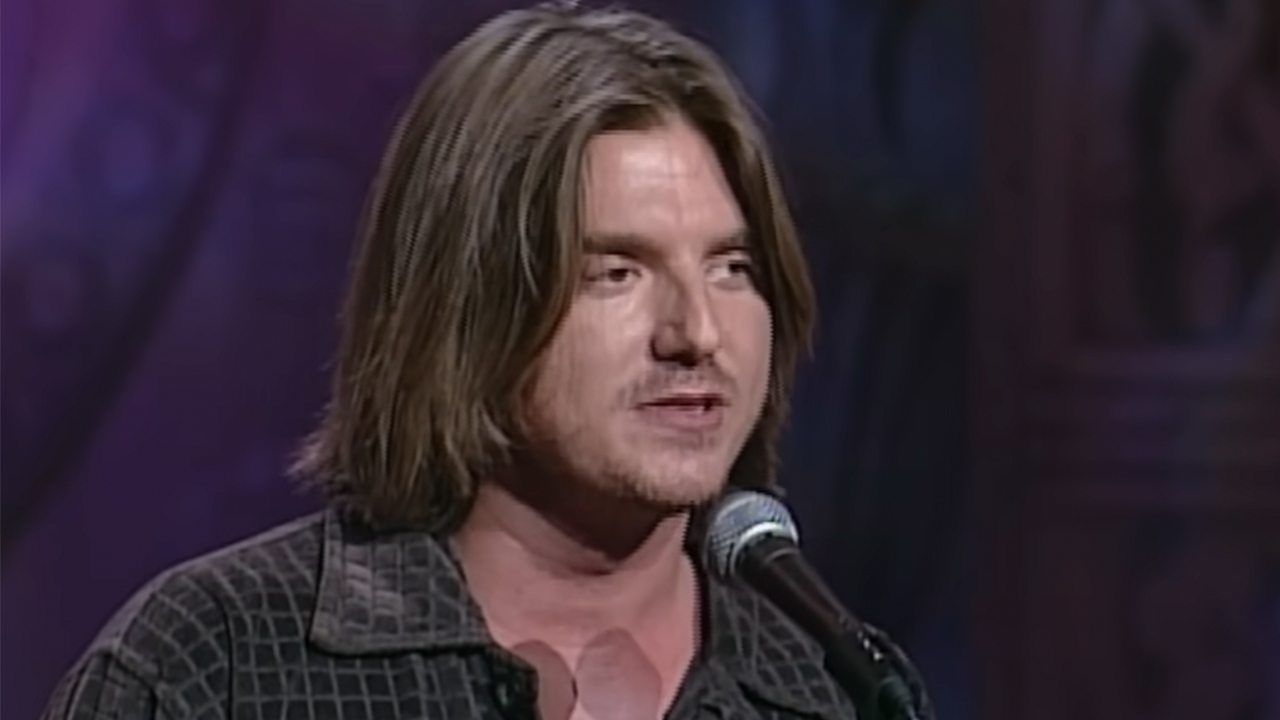 Mitch Hedberg, without sunglasses on, telling a joke on stage.