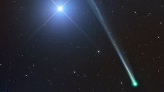 A bright comet is pictured to the lower right of a star-studded black sky. A tail extends diagonally upwards and away from the nucleus, past a bright blue star that dominates the left of the image, featuring prominent refraction spikes.