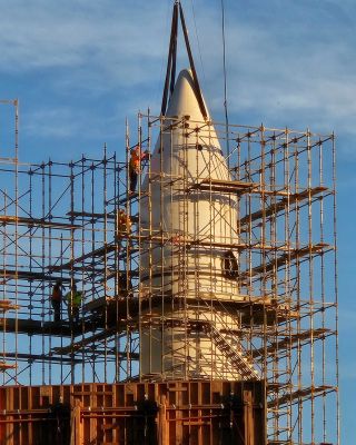 close-up view of the top of a white, conical rocket booster surrounded by scaffolding.
