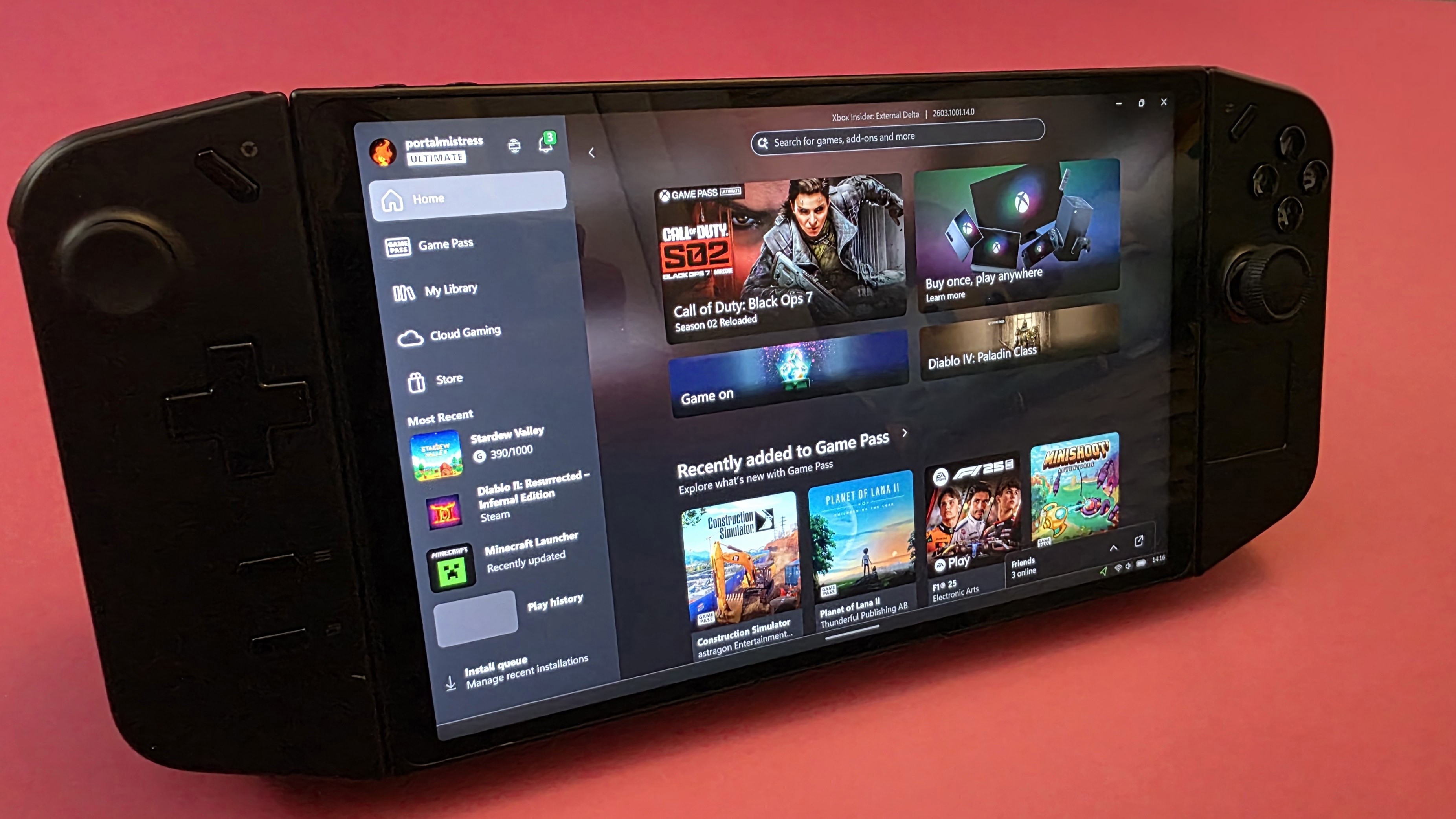 A handheld gaming device with a large screen and controls on each side rests on a pink surface.