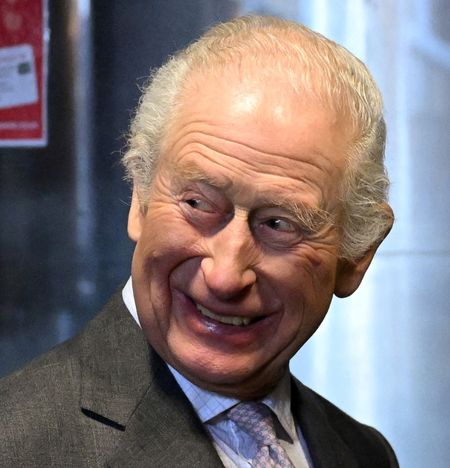 King Charles wearing a gray suit and smiling at a bar 