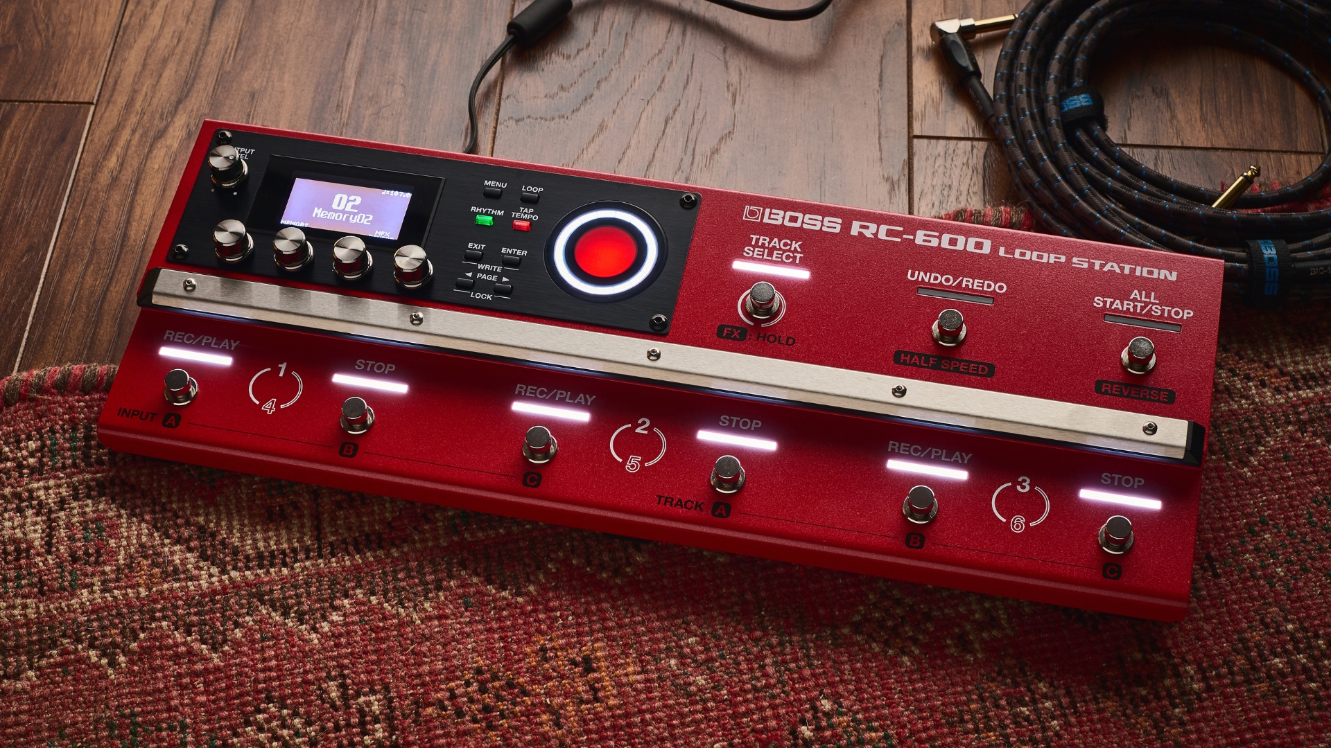 A Boss RC-600 looper pedal lying on a rug with some guitar cables nearby