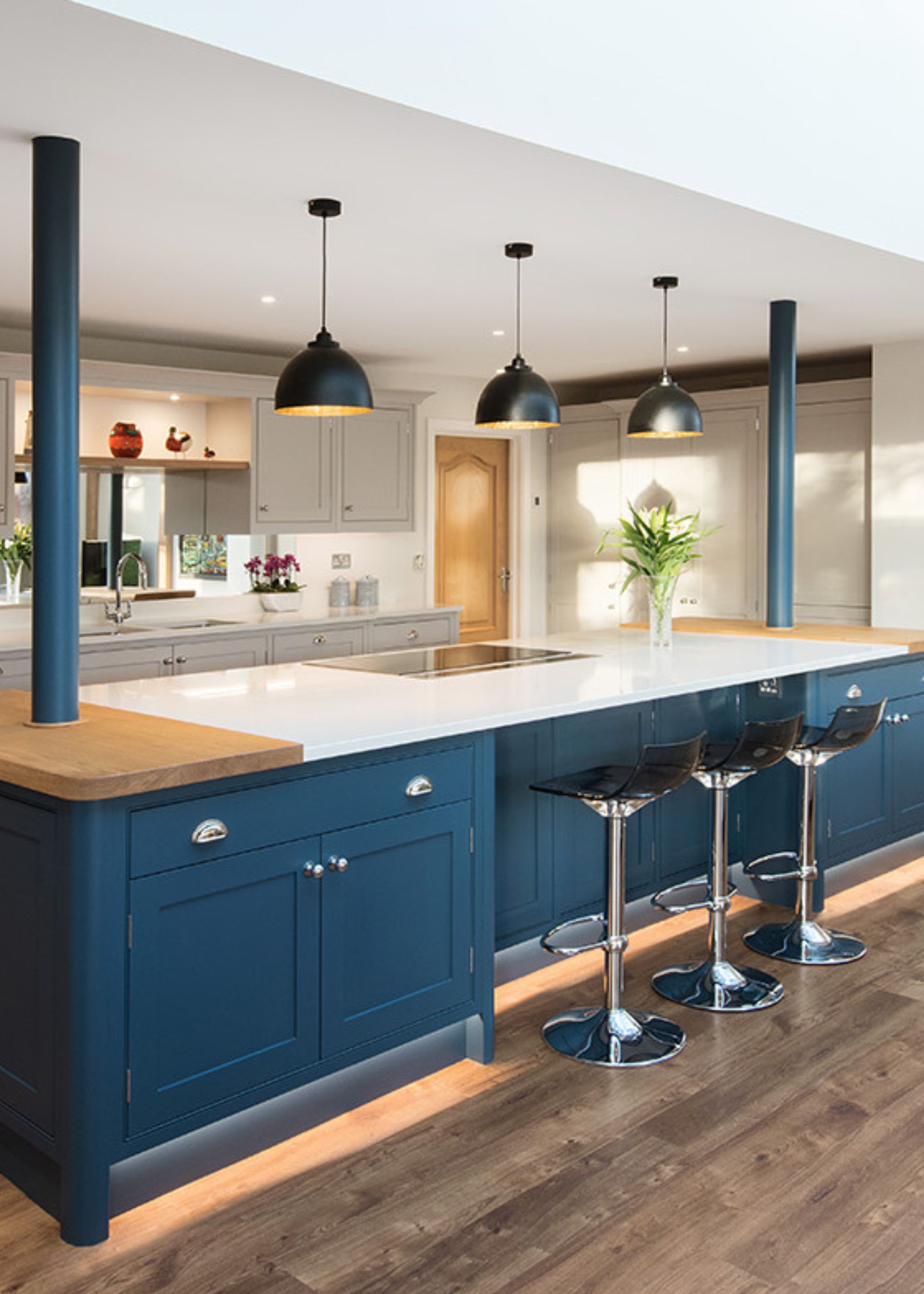 A chic navy blue and white kitchen with light pendants hanging above the island. Bar stools are also placed next to the Island.