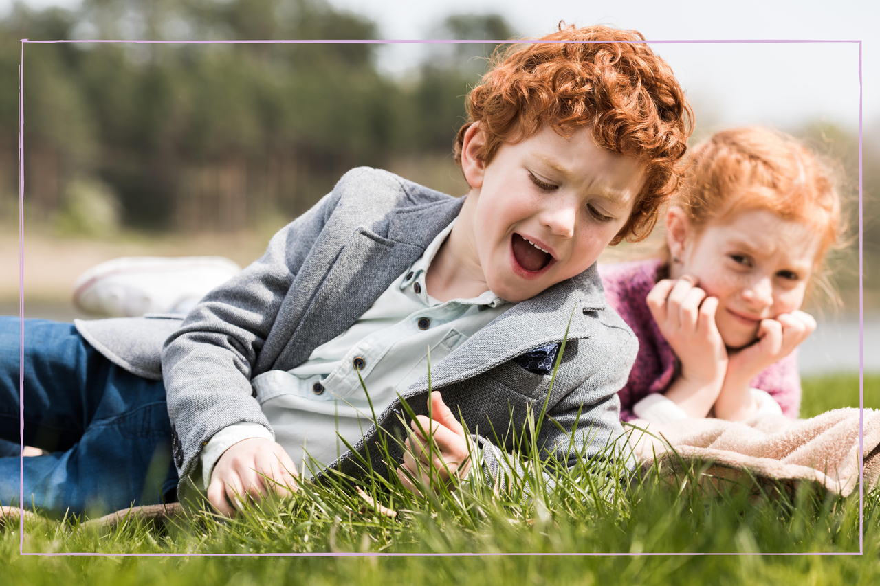 A brother and his younger sister laying on the grass on a sunny day