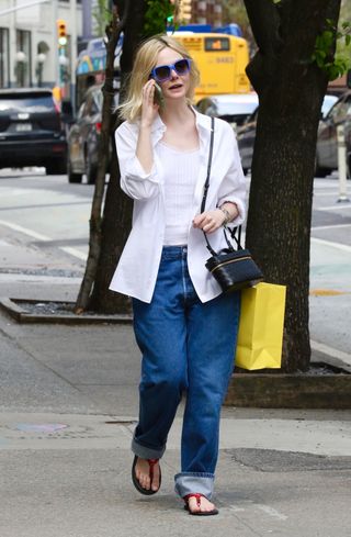 Elle Fanning berjalan di NYC mengenakan kemeja berkancing putih, jeans, sandal thong merah Miu Miu, dan tas Bottega Veneta Bang Bang.