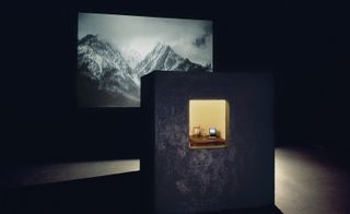 A dark room with a projected image of mountains on the wall. In front, is a tall rectangular object with an opening