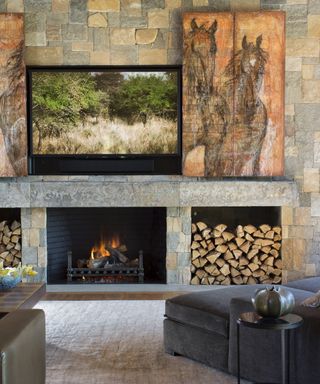 A living room with natural stone fireplace and artwork which opens to reveal a wall-mounted television