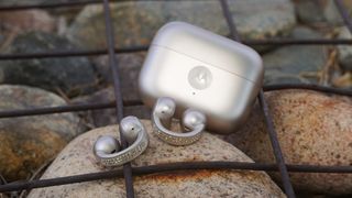 The Moto Buds Loop in PANTONE French Oak with Swarovski crystals on a rock beside their case.