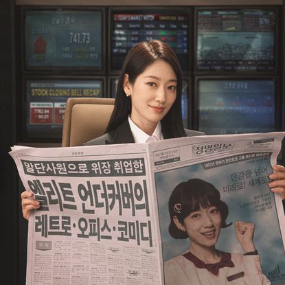 A woman (Park Shin-hye as Hong Keum-bo) holds up a Korean newspaper with a picture of herself with a younger hairstyle, in a promotional image from the Netflix K-drama 'Undercover Miss Hong.'