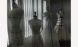 Four mannequins with different dresses on them and long vertical lights on the wall behind them.