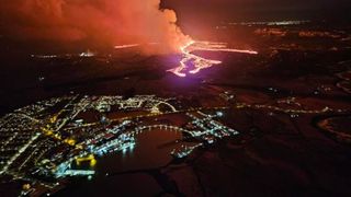 a glowing red river of fire flows next to city lights at night