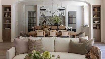 a view from the living room through to an open plan dining and kitchen space with a neutral couch front and center, a layered kitchen with marble backsplash and large island