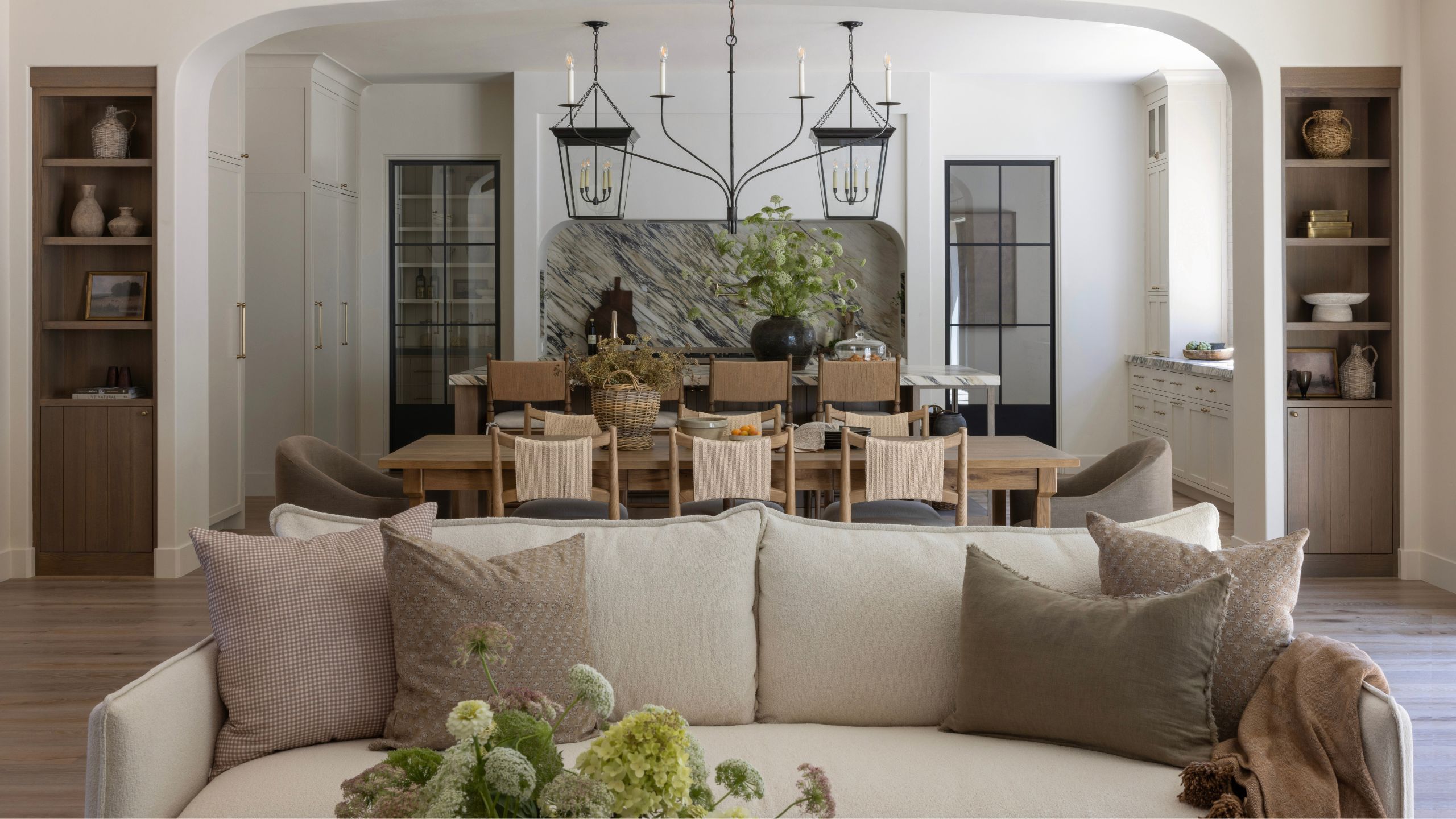a view from the living room through to an open plan dining and kitchen space with a neutral couch front and center, a layered kitchen with marble backsplash and large island