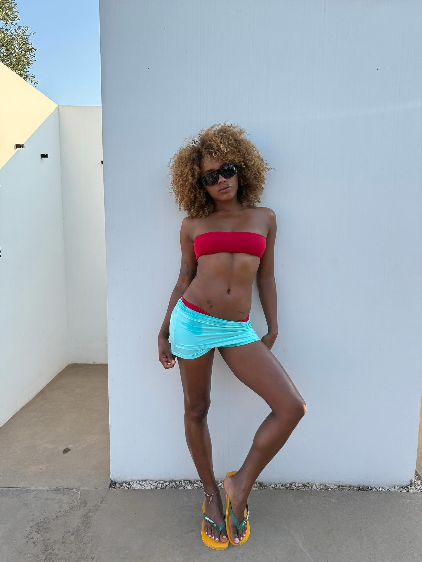 A woman wearing a bikini with a honey blonde, curly hairstyle