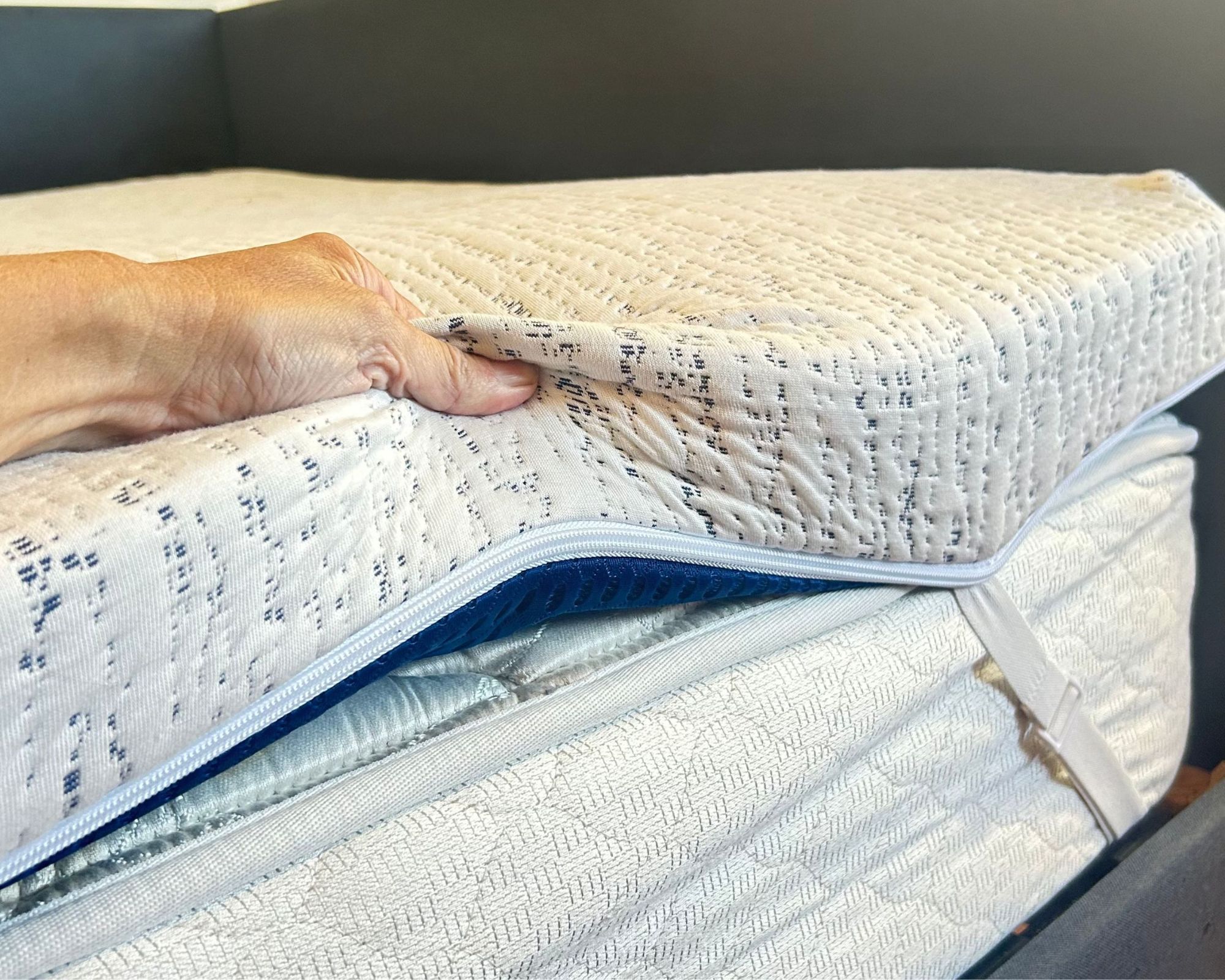 Testing the ViscoSoft High Density topper shown on a white mattress with white straps and a hand gripping the topper.