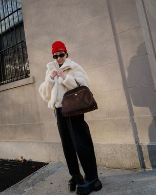 A woman wears black pants with a white fuzzy top and red hat in NYC.